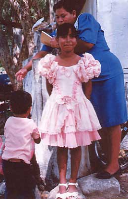 [Girl in pink dress getting last minute touchups to her hair by her mother and little brother outside their adobe home in Alamos, Sonora, Mexico: 18k]