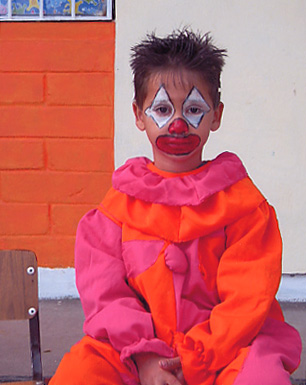 Little boy clown in pink and orange in front of an orange and white wall, waiting for the parade, Alamos, Sonora, Mexico