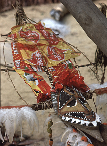 [wood yam mask decorated with bright red chip bags and flowers: 426k]